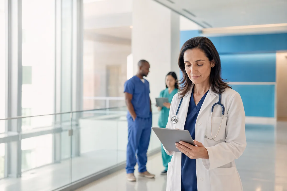 Physician reviewing a tablet in a bright hospital corridor